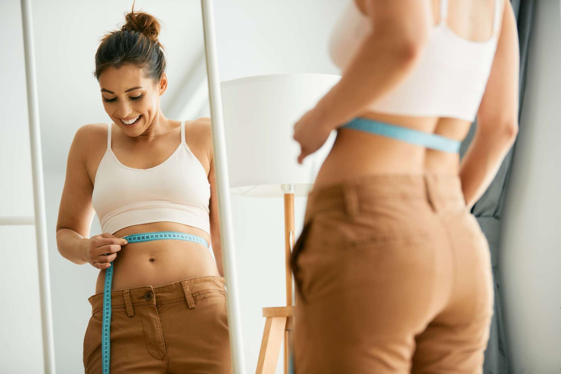 Happy Girl Measuring Her Waist With Measuring Tape In Front Of Mirror | Rachel Brown NP in Houston, TX